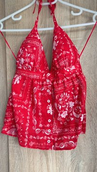 Top halter roșu cu modele florale și paisley. Dispune de un decolteu adânc în V, bretele ajustabile, talie strânsă și butoane albe. Material ușor.