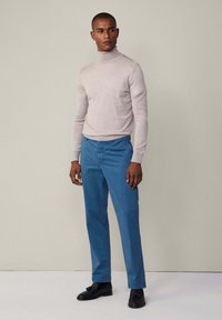 Svijetlosivi rolak, plave hlače, crne cipele. Gladak materijal s prilagođenim dizajnom, bez vidljivih uzoraka ili dodatnih detalja.