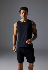 Top preto sem mangas feito de tecido macio, combinado com calções pretos. Design simples, com decote redondo e silhueta ajustada.