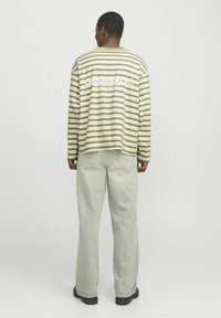 Camisa de manga larga a rayas en verde y blanco, con un corte relajado y un estampado gráfico en la parte posterior. Combinada con pantalones de denim claros.