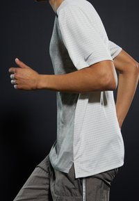 Lysegrå atletisk trøje med korte ærmer, tekstureret mønster og sideslidser. Har et lille Nike-logo på ærmet.