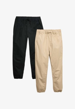 To par afslappede joggingbukser med elastiske linninger og snore, den ene i sort og den anden i beige, lagt fladt på en hvid baggrund.