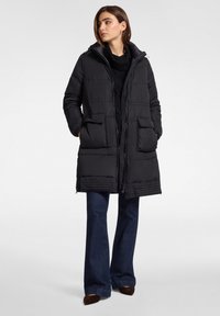 Czarna pikowana kurtka z przodu na zamek, z kapturem i dwoma przednimi kieszeniami. Charakteryzuje się pikowaną fakturą i ściągaczem u dołu. Połączona z ciemnoniebieskimi dzwonowatymi jeansami.