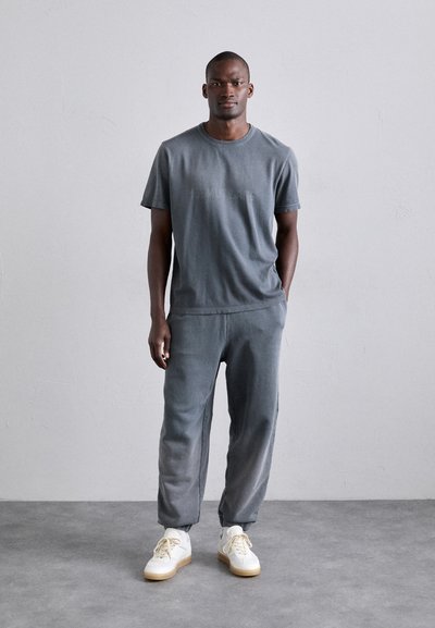 Grå bomull t-skjorte og matchende joggebukser med avslappet passform. Teksturert stoff, subtil merkebranding på skjorten, kombinert med hvite sneakers.