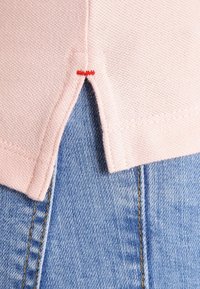 Růžová pletenina se strukturovaným vzorem má rozdělený lem. Níže je vidět světle modrý denim s žlutým prošíváním.