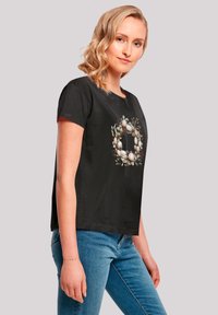Black cotton t-shirt featuring a floral wreath design with eggs, short sleeves, and a relaxed fit. Smooth texture, rounded neckline.