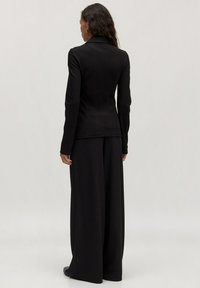 Zwarte getailleerde blazer met een gestructureerde pasvorm, lange mouwen en een zachte textuur, gecombineerd met zwarte wijduitlopende broeken.