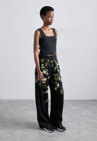 Sort ærmeløs top med firkantet udskæring parret med brede sorte bukser med grønne blomster mønstre og elastisk talje.
