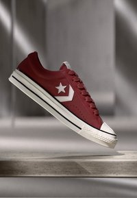 Red leather sneaker featuring a white star logo, perforated side panel, and black striped sole. Rounded toe with a classic lace-up design.