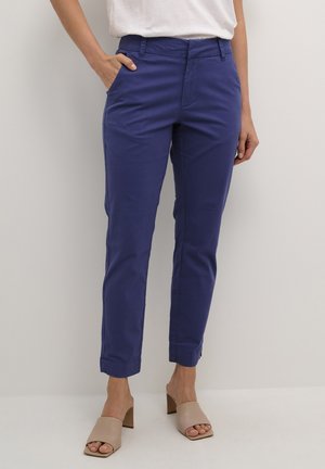 Blauwe katoenen broek met slim fit, voorkruiken en opgerolde uiteinden. Gecombineerd met beige instapsandalen voor een casual look.