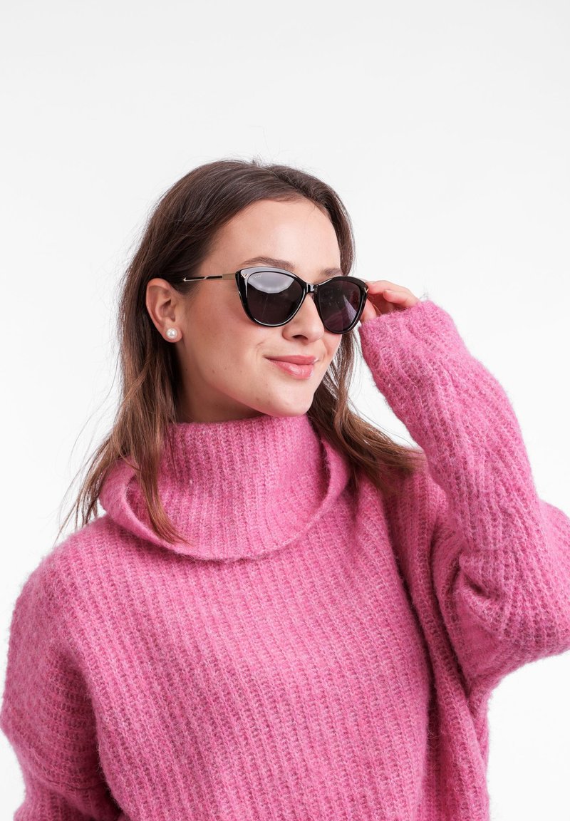 Flauschiger rosa Strickrollkragenpullover mit lockeren Ärmeln, kombiniert mit schwarzen Katzenaugen-Sonnenbrillen, die eine glatte Textur und einen kräftigen Farbkontrast betonen.