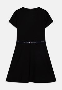 Czarna sukienka z krótkim rękawem, z rozkloszowanym dołem i granatową elastyczną talią z napisem "TOMMY HILFIGER" w białym kolorze. Gładka faktura materiału.