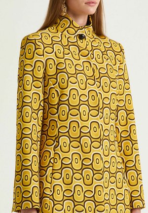 Long-sleeved jacket in a vibrant yellow fabric featuring a geometric brown and white pattern, high collar, and a black button closure.