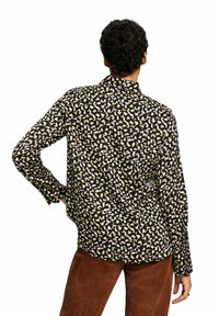 Zwarte blouse met een luipaardprint in geel, crème en wit. Lange mouwen en een klassieke kraag. Zacht materiaal met een ontspannen fit.