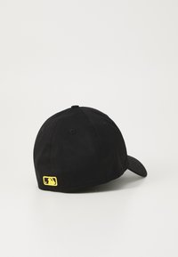Juodas baseballo kepurė, pagaminta iš audinio su išlenktu kraštu, su mažu geltonu logotipu ant nugaros. Lygi tekstūra, suapvalinta forma.