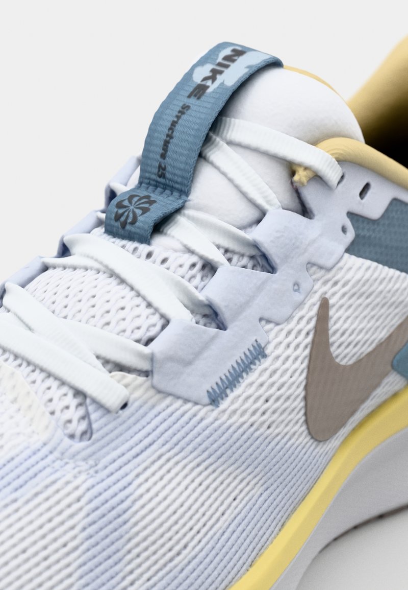 Zapatilla azul claro con parte superior de malla texturizada, suaves acentos amarillos, un distintivo cierre de cordones azul y un logo de Nike en beige.