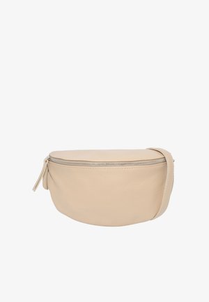 Junge Frau mit langen braunen Haaren lächelt, trägt ein schwarzes Oberteil, schwarze Lederhose und eine beige Umhängetasche mit Reißverschluss.