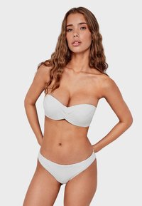 Ensemble de bikini blanc comprenant un haut bandeau avec un motif ondulé texturé et un bas taille basse assorti, tous deux fabriqués en tissu lisse.