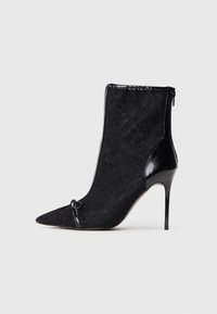 Sort ankelstøvle med spidse tæer, tekstureret stofoverdel, shiny sorte patentdetaljer og en stiletto hæl. Låses med lynlås i siden.