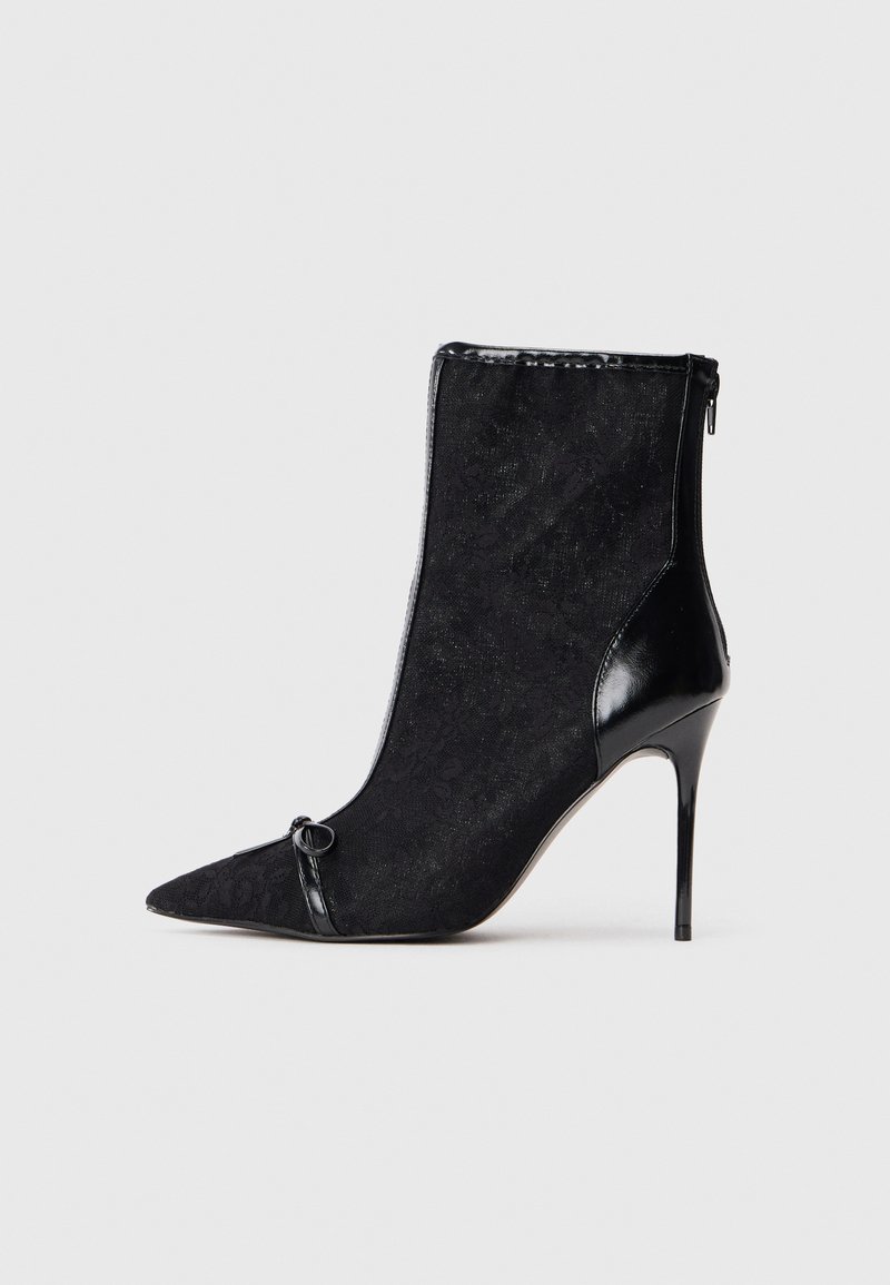 Sort ankelstøvle med spidse tæer, tekstureret stofoverdel, shiny sorte patentdetaljer og en stiletto hæl. Låses med lynlås i siden.