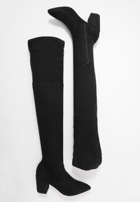 Sorte over-knee-støvler lavet af blødt ruskind, med spids tå, kraftig hæl og en lynlås i siden for nem påtagning.