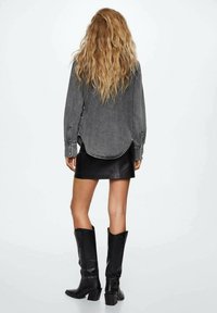 Veste en denim gris à manches longues, ourlet arrondi et fentes latérales, associée à une mini-jupe en cuir noire et des bottes noires montantes jusqu'aux genoux.