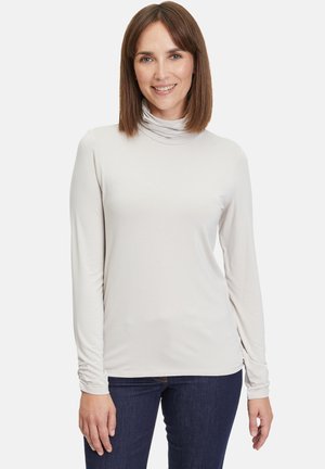 Helles graues Longsleeve mit Rollkragen aus weichem, dehnbarem Stoff, mit gerafften Details an den Bündchen, kombiniert mit dunkelblauen Jeans.