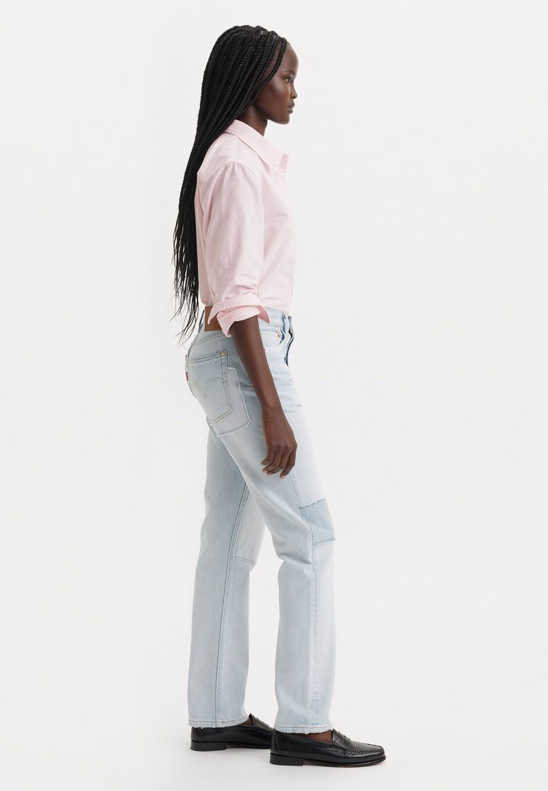Jeans in denim azzurro chiaro con una vestibilità comoda, abbinati a una camicia button-up rosa chiaro. Gli accessori includono mocassini neri.