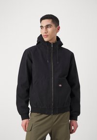 Juodas zip-up džemperis su kapišonu, pagamintas iš tekstūruoto audinio, su kengūros kišene ir elastingomis rankovėmis. Papuoštas mažu logotipu.