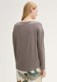 Grijs lange mouwen top gemaakt van gladde stof met een ronde halslijn en verlaagde schouders, gecombineerd met een patroon van beige en groene broek.