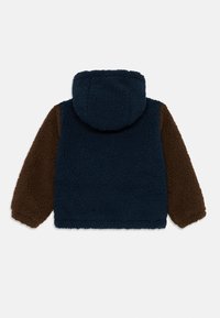 Veste en polaire à capuche avec un corps bleu marine et des manches marron, dotée d'un tissu doux et texturé ainsi que de poignets élastiques.
