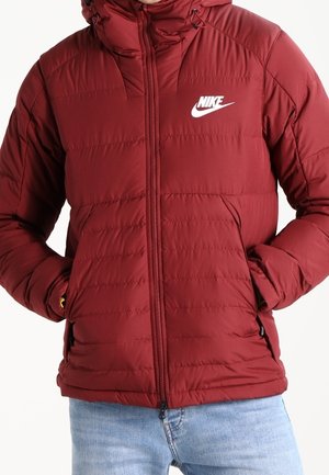 Maroon puffer jacket with a zip closure, padded design, high collar, and logo accent on the upper left. Features side pockets.