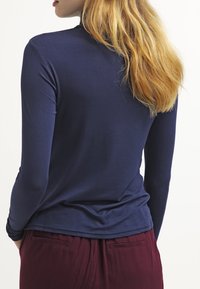 Námořnická dlouhá rukávová mikina vyrobená z měkké tkaniny, s přiléhavým střihem a hladkou texturou, v kombinaci s bordovými kalhotami s bočními kapsami.