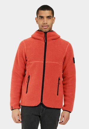 Rote Fleecejacke mit hohem Kragen, ausgestattet mit einem schwarzen Reißverschluss und zwei Fronttaschen. Die Textur ist weich und kuschelig, mit schwarzen Akzenten.