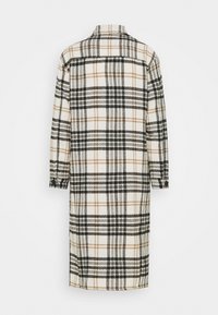 Cappotto lungo a quadri con una combinazione di colori crema, nero e marrone. Realizzato in tessuto strutturato con collo e maniche con bottoni.