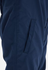 Navyblauwe stoffen broek met een gladde textuur, voorzien van een zijzak en een rechte snit, benadrukt door strakke stiksels.
