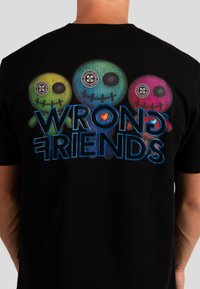 Czarny t-shirt z trzema kolorowymi rysunkami czaszek w kolorach zielonym, niebieskim i różowym, z napisem "WRONG FRIENDS" poniżej w kolorze niebieskim.