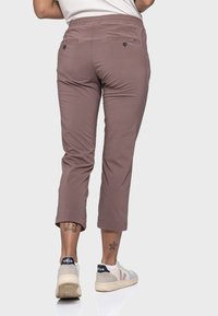 Braune, knöchellange Hose mit einem dehnbaren Bund, zwei Gesäßtaschen und aufgerollten Hosenenden. Kombiniert mit grauen und weißen Sneakers.