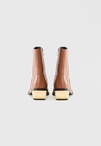 Botine maro cu finisaj lucios, fermoare laterale și tocuri bloc aurii în contrast. Textură netedă și design elegant.
