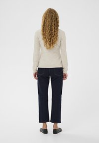 Šviesiai smėlio spalvos megztinis, mėlyni tiesaus kirpimo džinsai, juodi batai be kulnų. Megztinis turi ilgus rankovus; džinsai išsiskiria penkių kišenių dizainu ir kontrastinga siūle.