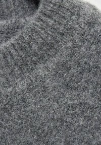 Gros plan d’un tissu en laine gris doux et épais avec une texture duveteuse et un motif de tricot visible.