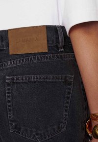 Tumedad denim püksid, mille taga on nahkplekk "LAMANIA", lähedalt vaadates õmblusi ja tasku detaile.