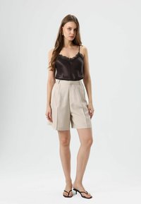 Caraco en satin noir avec bordure en dentelle associé à un short taille haute beige, orné de plis et d'une coupe décontractée. Porté avec des sandales noires.