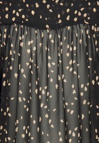 Černé šaty s texturovaným vrškem a splývavou sukní. Sukně má nepravidelný béžový puntíkový vzor na poloprůsvidné látce.