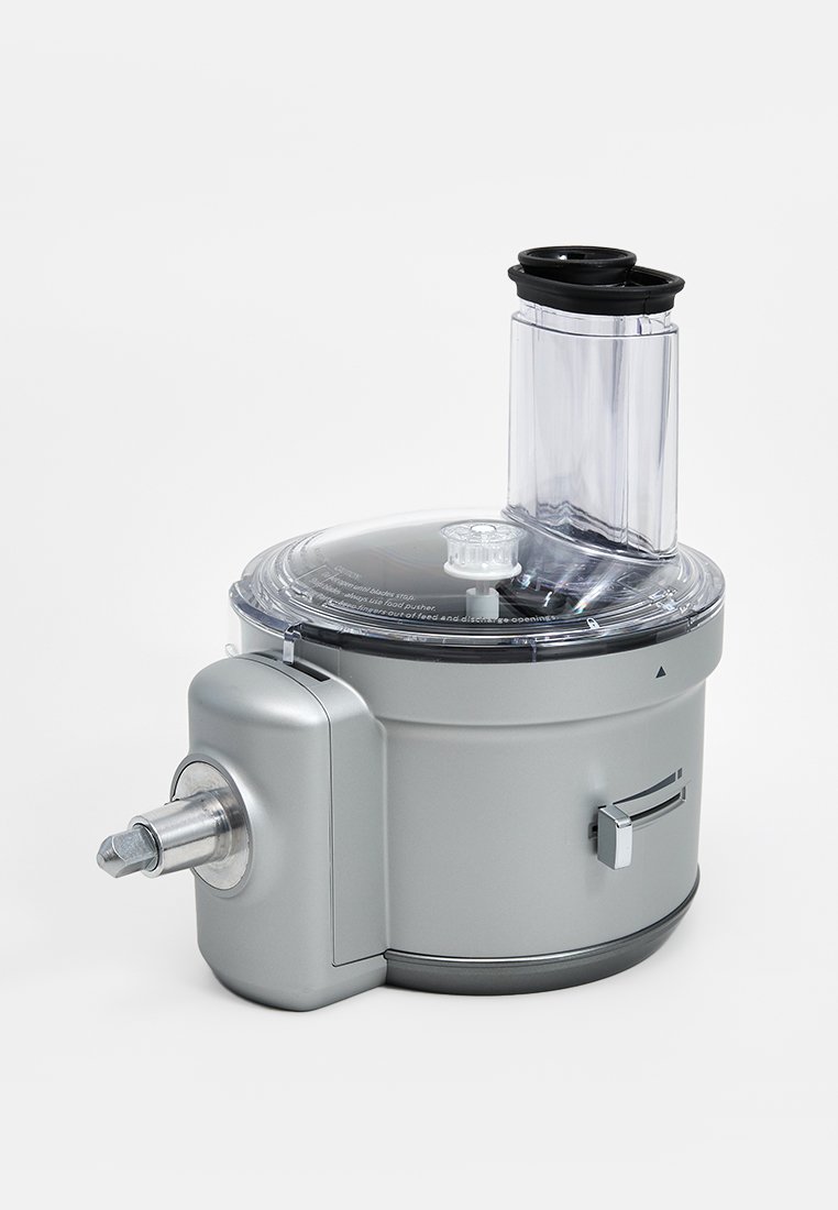 Hachoir avec un boîtier en métal argenté, un couvercle en plastique transparent et un tube d'alimentation vertical. Il dispose d'une sortie en acier inoxydable et de boutons de commande.