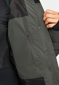 Ciemnozielona kurtka ocieplana z kontrastową czarną wstawką. Posiada zasuwaną kieszeń po lewej stronie oraz zatrzaski z przodu.