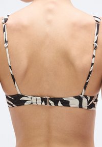 Bagfra visning af en sort-hvid mønstret bikinioverdel med justerbare stropper, lukning med krog og tekstureret stof.