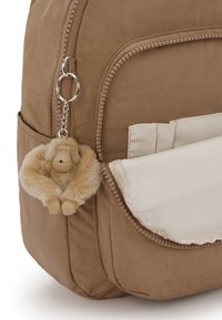 Zaino in tessuto marrone con chiusura a cerniera, tasca frontale e portachiavi a forma di scimmia in peluche attaccato. Texture liscia con accenti in contrasto.