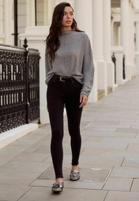 Pilka ilgomis rankovėmis palaidinė, juodos siauro kirpimo kelnės ir raštuotos laisvalaikio bateliai. Apranga pasižymi laisvu siluetu ir neutraliais atspalviais, turinčiais tekstūruotą paviršių.