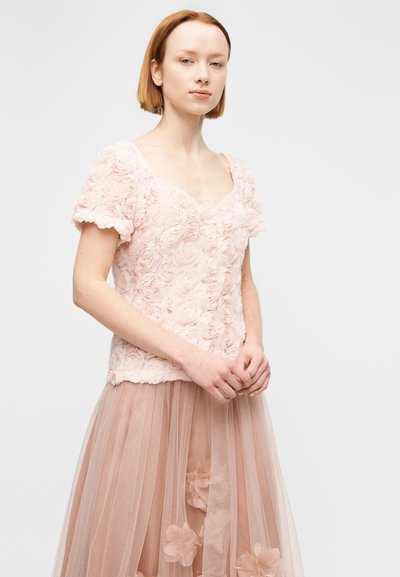Απαλό ροζ λουλουδάτο τοπ με κοντά μανίκια, υφασμάτινα τριανταφυλλένια εφαρμογές, σε συνδυασμό με μια στρωματοποιημένη, διάφανη φούστα με λουλουδάτες λεπτομέρειες.
